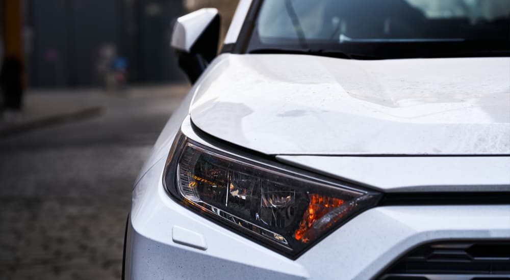 A close up of the headlight and hood of a silver Toyota RAV4 is shown.