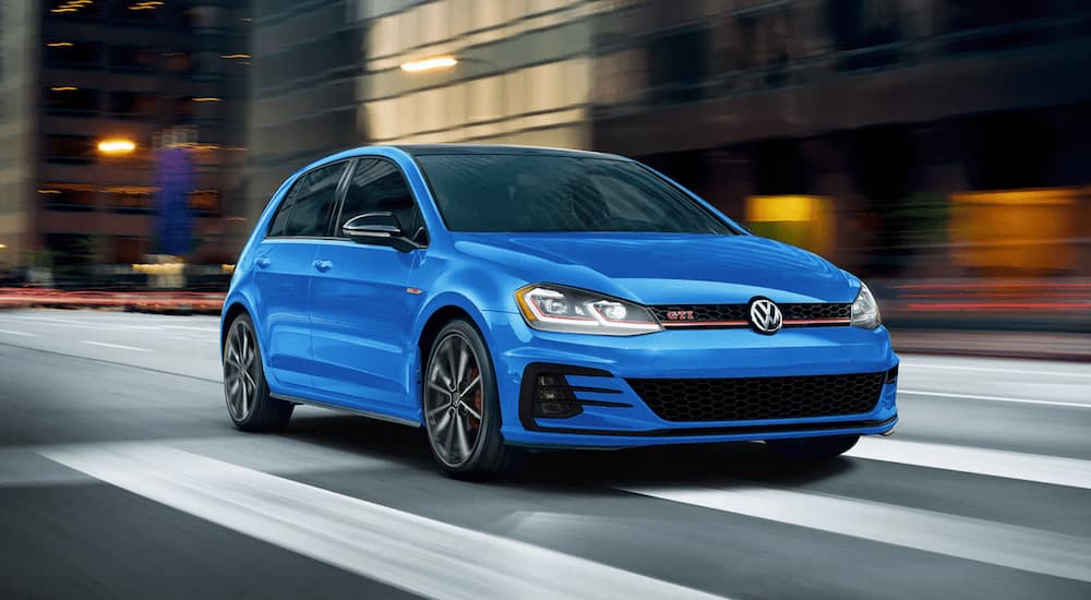 A blue 2021 Volkswagen Golf GTI is shown from the front driving through a city.