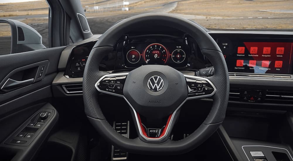 The black interior of a 2022 Volkswagen Golf GTI shows the steering wheel and infotainment screen after leaving a VW dealer.