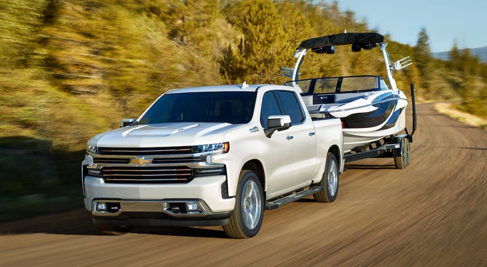 A popular certified pre-owned Chevy Silverado, a white 2020 Chevy Silverado 1500 High Country is shown towing a boat on an open road.