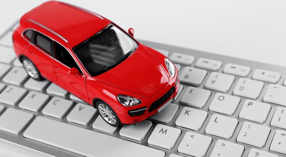 A toy car is shown resting on a computer keyboard at an online car dealer.