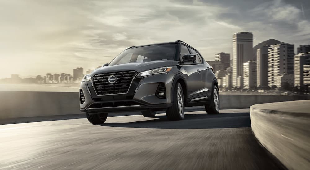 A grey 2021 Nissan Kicks is shown from the front driving on an open road out of the city.