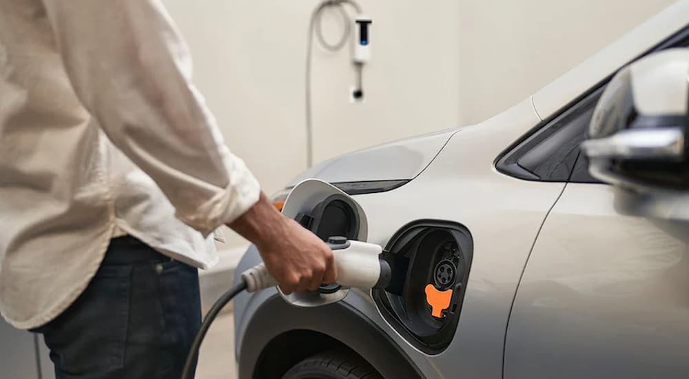 A close up of a person plugging in a 2022 Chevy Bolt EV into a home charger is shown.