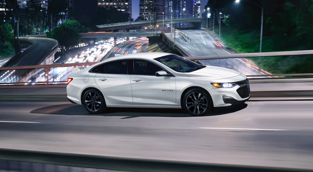 A white 2022 Chevy Malibu is shown from the side driving on a city street.