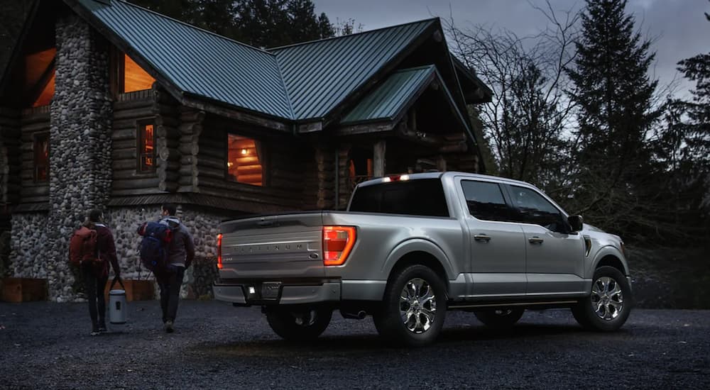 A silver 2022 Ford F-150 is shown from the side parked in front of a log cabin.