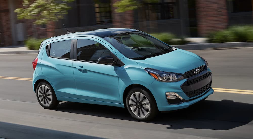 A turquoise 2022 Chevy Spark  is shown from the side driving on a city street.