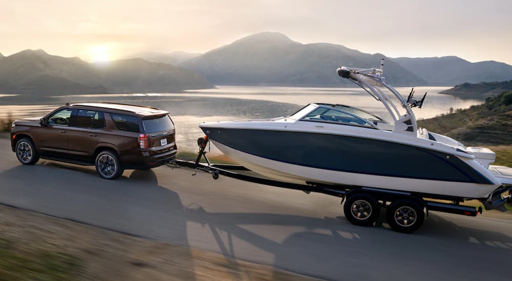 A brown 2022 Chevy Tahoe is shown towing a boat past a lake.
