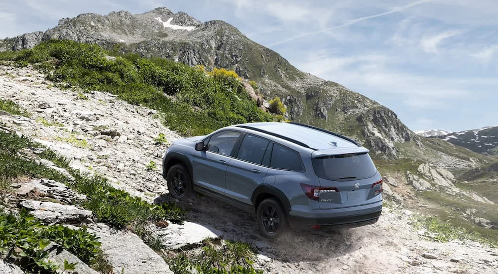 A grey 2022 Honda Pilot Trailsport is shown from a rear angle driving up a rocky path.