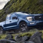 A blue 2022 Ford F-150 is shown from the side driving on the side of a mountain after leaving a used truck dealership in Albany.