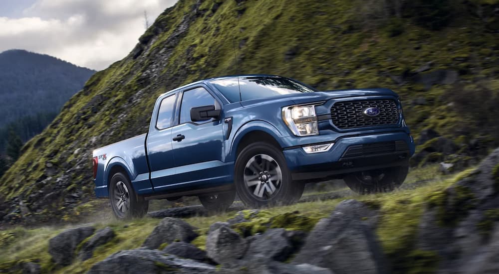 A blue 2022 Ford F-150 is shown from the side driving on the side of a mountain after leaving a used truck dealership in Albany.