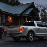 A grey 2022 Ford F-150 is shown from the side parked in front of a log cabin.