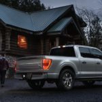 A grey 2022 Ford F-150 is shown from the side parked in front of a log cabin.