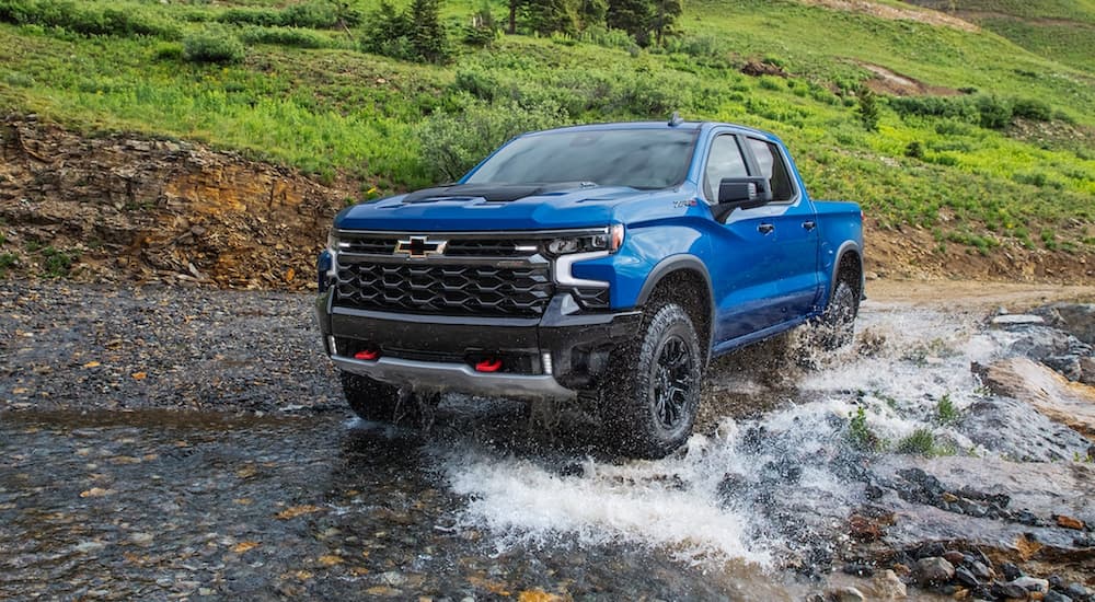 A blue 2022 Chevy Silverado 1500 ZR2 is shown off-roading through a river.