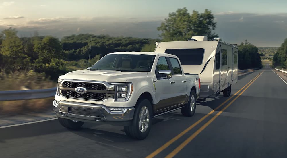 A white 2022 Ford F-150 is shown towing a camper trailer on an open road.