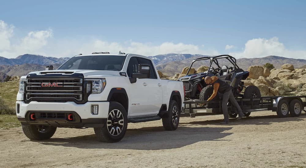 A white 2022 GMC Sierra 2500HD is shown from the front towing a trailer loaded with a side by side after winning a 2022 GMC Sierra 2500HD vs 2022 Chevy Silverado 2500 HD comparison.