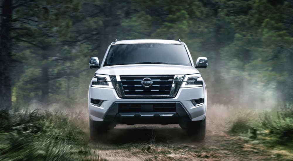 A white 2022 Nissan Armada is shown from the front off-roading on a dirt road through a forest.