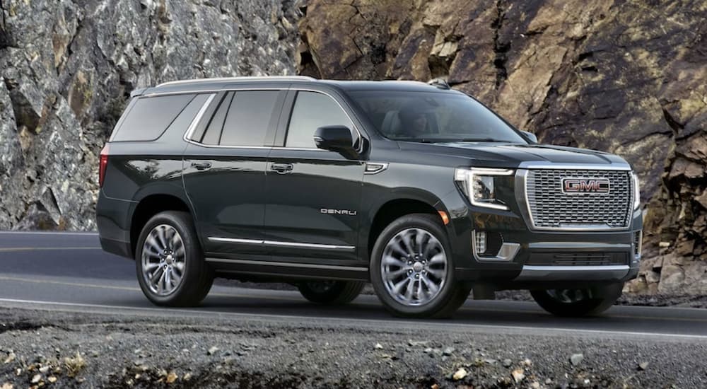 A green 2022 GMC Yukon Denali is shown from the side parked in front of a rock.