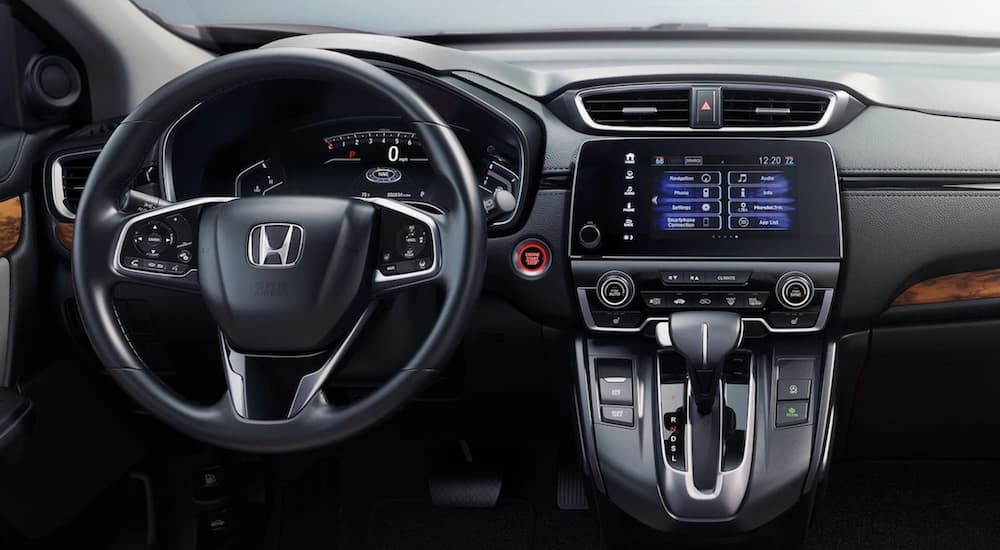 The black interior of a 2022 Honda CR-V Hybrid Touring shows the steering wheel and infotainment screen.