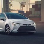 A silver 2022 Toyota Corolla Hybrid LE is shown from the front parked at a shipping container lot.