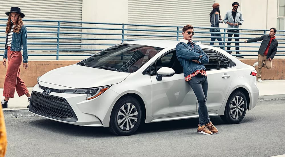 A white 2022 Toyota Corolla Hybrid LE is shown from the side parked ina city as a person leans on the vehicle.