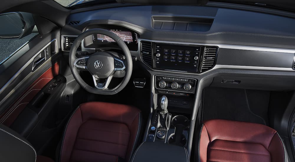 The black and red interior of a 2022 Volkswagen Atlas Cross Sport V6 SEL Premium R-Line shows the steering wheel and infotainment screen.