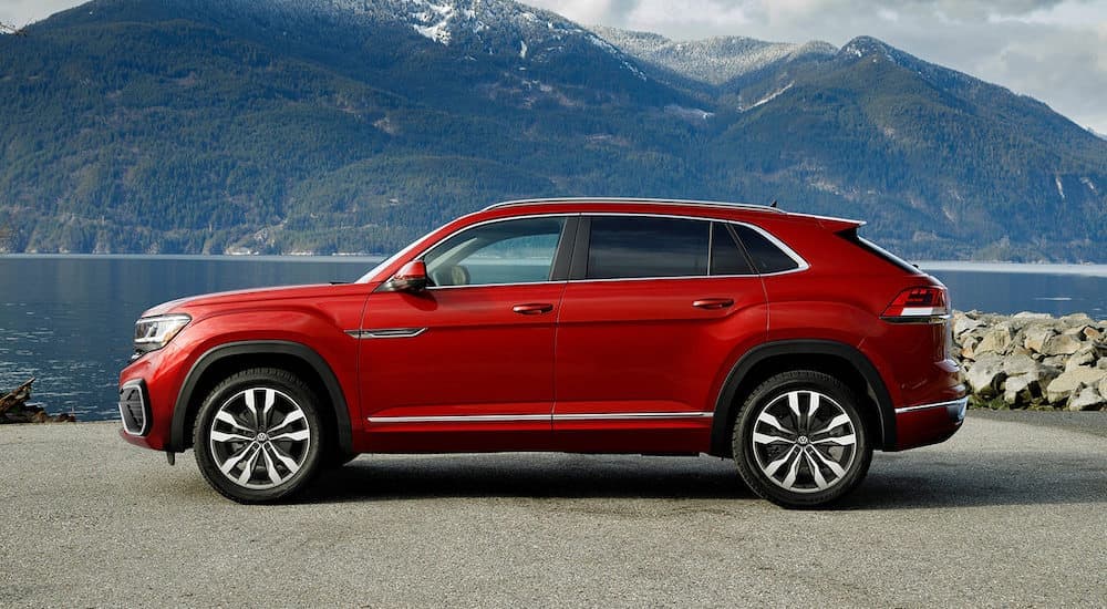 A red 2022 Volkswagen Atlas Cross Sport V6 SEL Premium R-Line is shown from the side parked in front of a lake and mountain.