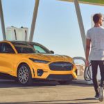 A yellow 2022 Ford Mustang Mach-E is shown at a charger with the owner approaching after he searched "Ford dealer near me".