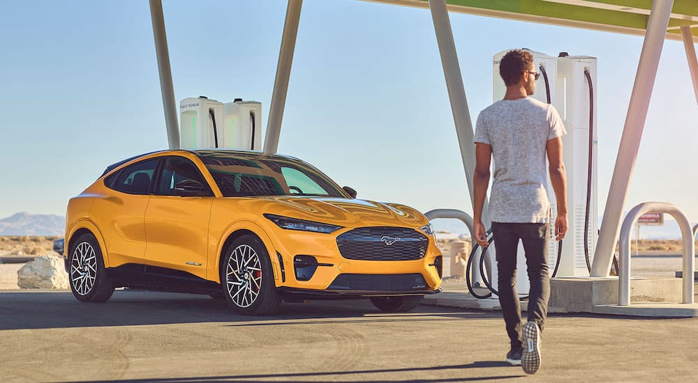 A yellow 2022 Ford Mustang Mach-E is shown at a charger with the owner approaching after he searched "Ford dealer near me".