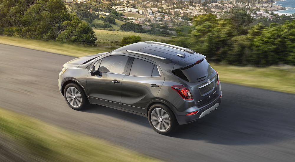 A grey 2017 Buick Encore is shown from the side driving on a road overlooking a small town.