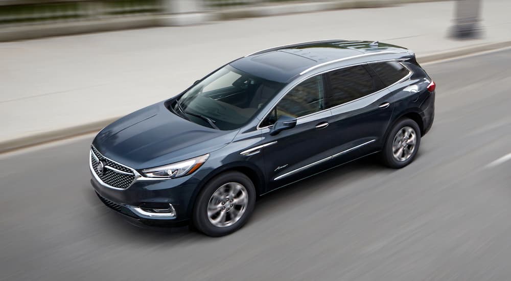 A blue 2018 Buick Enclave Avenir is shown leaving a certified pre-owned Buick dealer.