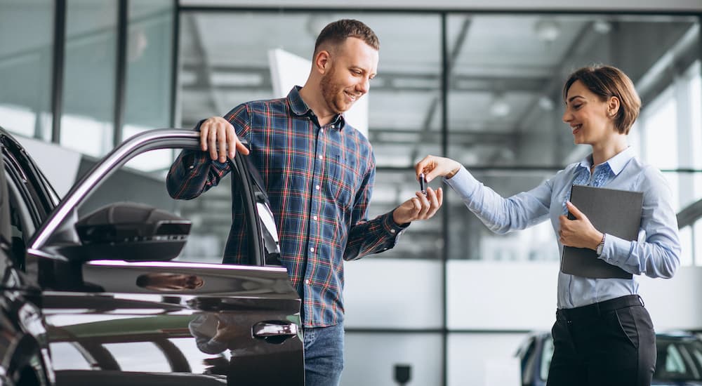 A salesperson is shown handing a set up keys to a customer exiting a vehicle.