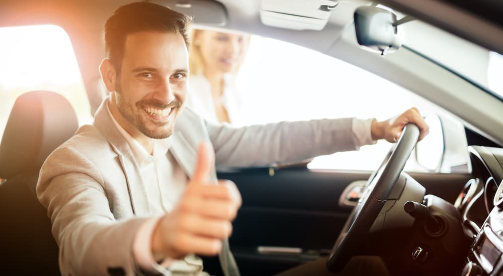 A person is giving a thumbs up while sitting in the front seat of a car.