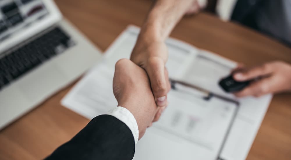 A person is shown shaking hands over paperwork at a Certified Pre-Owned Ford dealer.