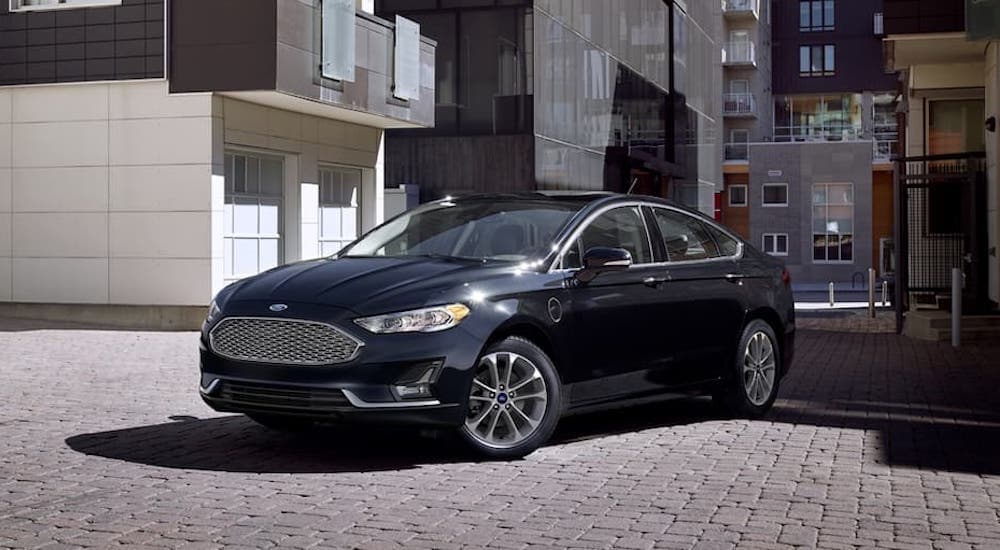 A black 2019 Ford Fusion is shown from the side parked in front of a building.