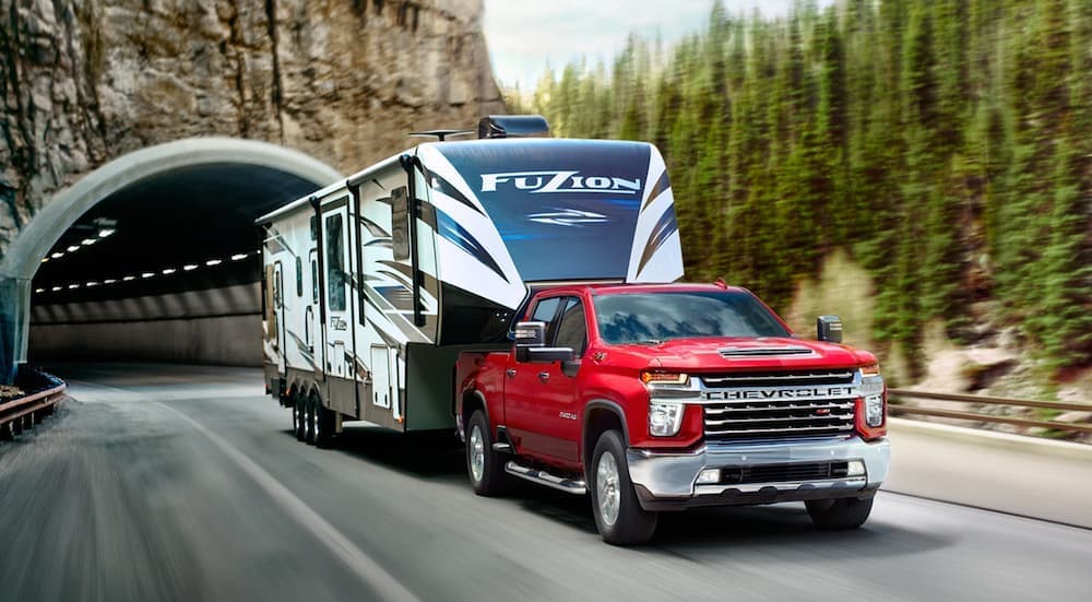A red 2020 Chevy Silverado 2500HD is shown towing a camper after leaving a Certified Pre-Owned vehicle dealer.