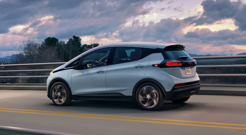 A blue 2022 Chevy Bolt EV is shown from the side driving on an open road at sunset.