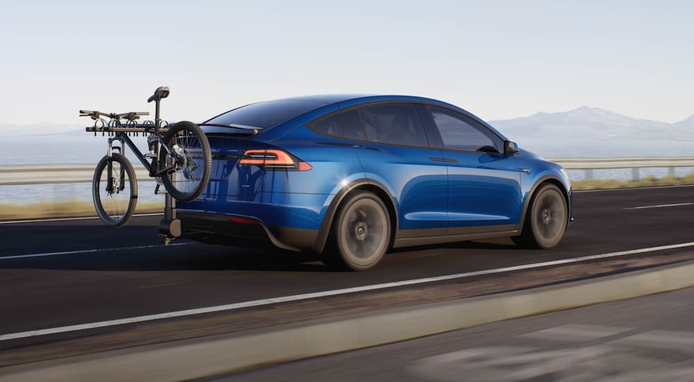 A blue 2022 Tesla Model X is shown driving on an open road.