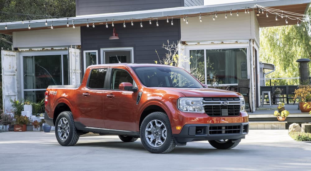 An orange 2022 Ford Maverick Lariat is shown from the front at an angle parked in front of a house.