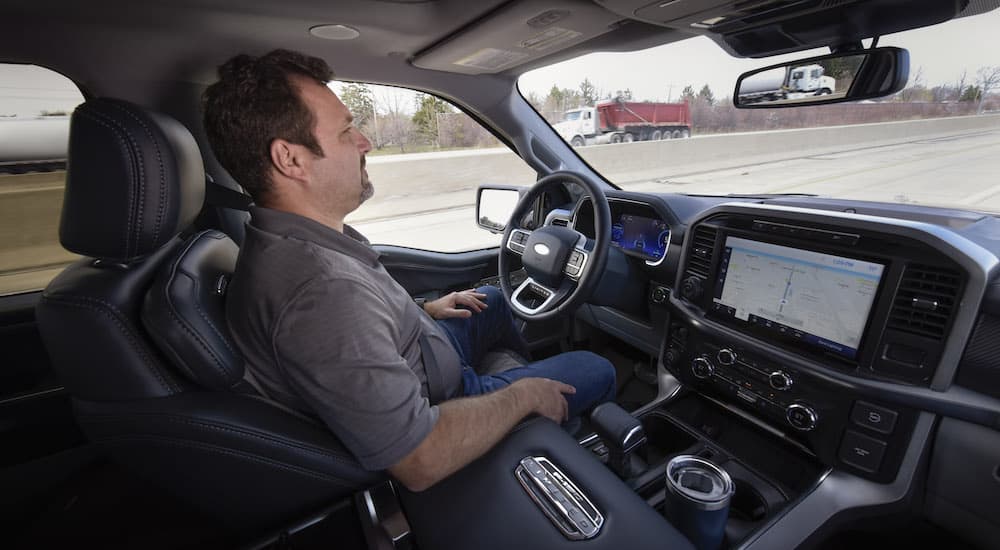 A man is shown sitting in the drivers seat of a Ford vehicle while test driving Ford's BlueCruise at a Ford dealer.