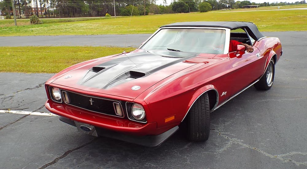 A red 1973 Ford Mustang is shown from the front parked on pavement at a Ford dealership.