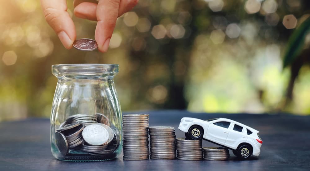 A white toy car is shown driving up stacks of coins.