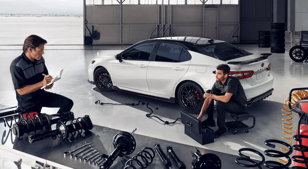 Mechanics are shown working on a white 2022 Toyota Camry TRD at a Toyota Camry dealer.