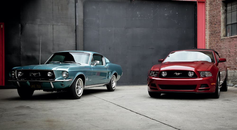 A blue 1967 Ford Mustang Fastback is shown parked next to a red 2014 GT in an alley.