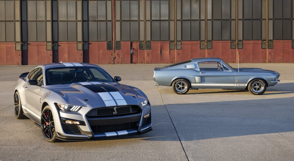 A grey 2022 Ford Mustang GT500 Heritage Edition is shown parked next to a blue 1967 Mustang GT500 outside of a warehouse.