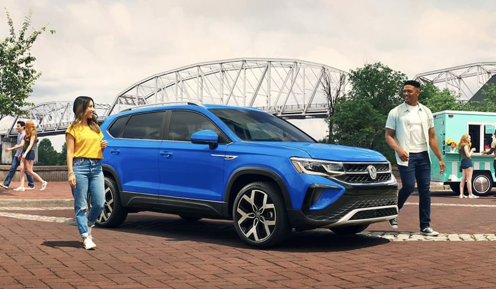 A blue 2022 Volkswagen Taos is shown from the side parked in front of a bridge.