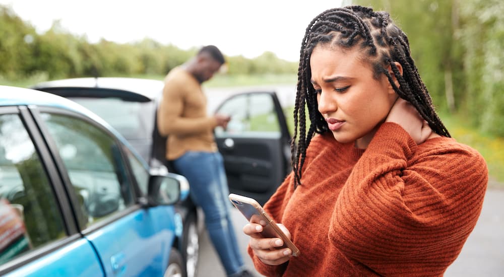 A woman is shown looking concerned at her phone scheduling a collision repair after getting into a collision.