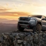 A 2022 Nissan Frontier Pro-4x is shown from the front at an angle driving over a rocky outcrop after searching "Nissan dealer near me".