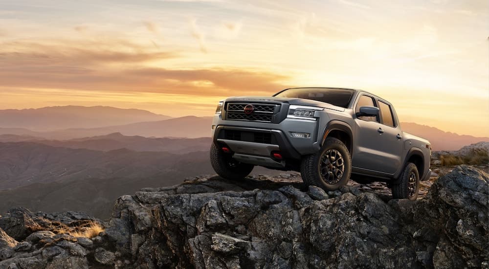 A 2022 Nissan Frontier Pro-4x is shown from the front at an angle driving over a rocky outcrop after searching "Nissan dealer near me".