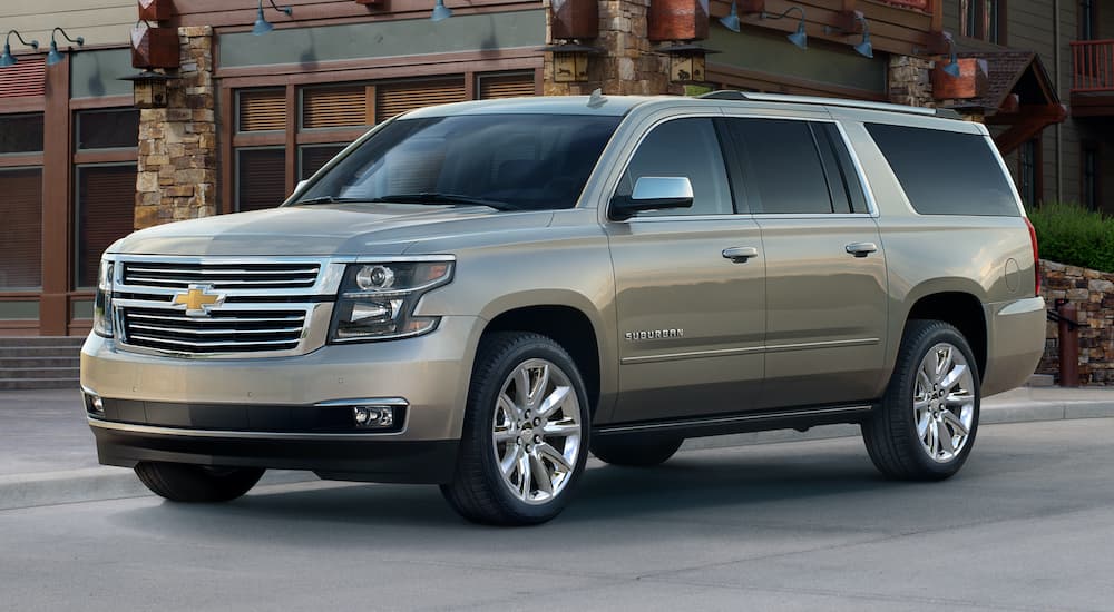 A tan 2018 Chevy Suburban is shown from the side parked in front of a modern building.