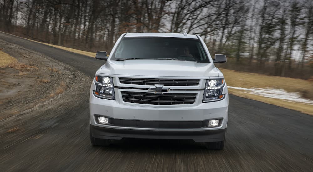 A white 2018 Chevy Tahoe RST is shown from the front driving on an open road past a used Chevy Tahoe dealer.